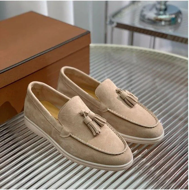 Scarpe mocassini beige in pelle scamosciata con nappine, su tavolo di vetro, scatola marrone sullo sfondo. Eleganti, casual, moda uomo.