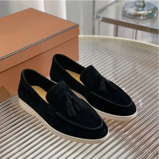 Mocassini neri in velluto con nappine su tavolo di vetro, scatola marrone sullo sfondo. Scarpe eleganti uomo, moda calzature di lusso.