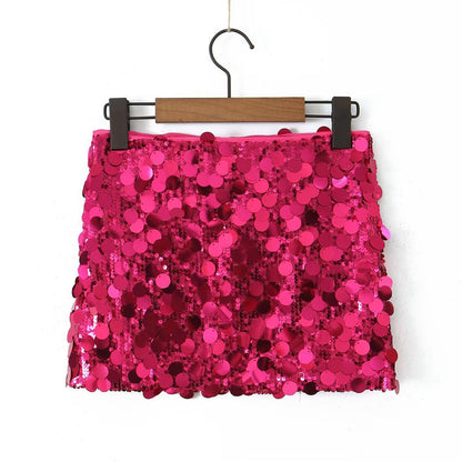 Gonna mini rosa con paillettes scintillanti, appesa su gruccia di legno. Moda femminile, abbigliamento da festa, stile glamour.