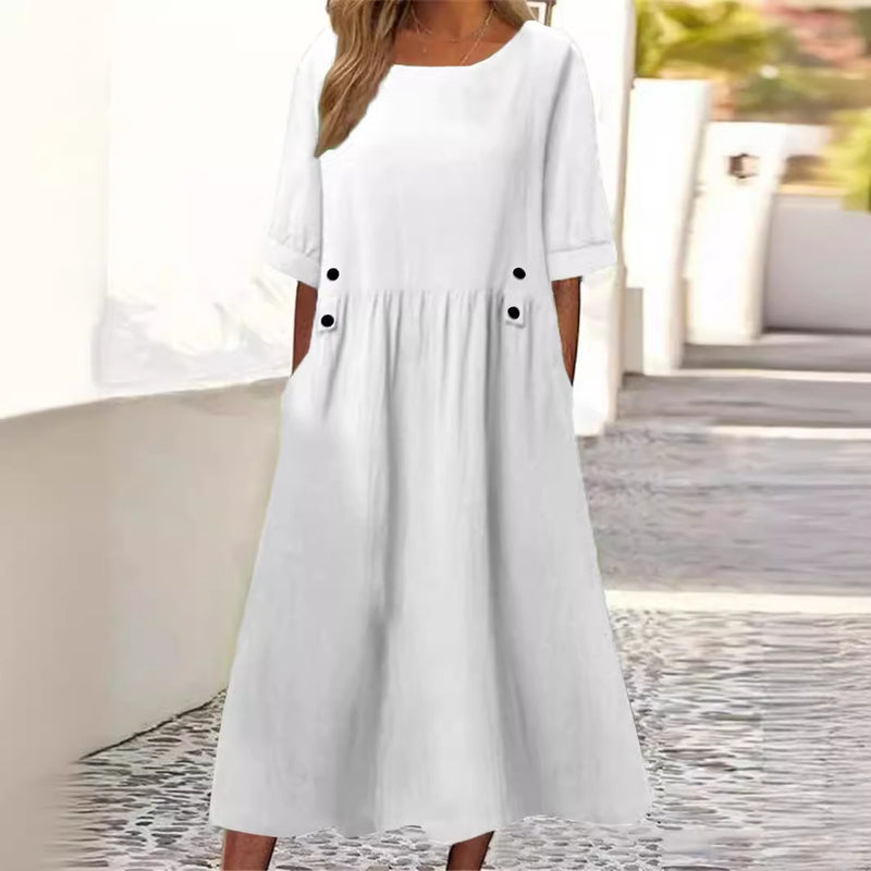 Abito bianco estivo da donna con maniche corte e tasche, design casual ed elegante, perfetto per giornate calde. Sfondo urbano luminoso.