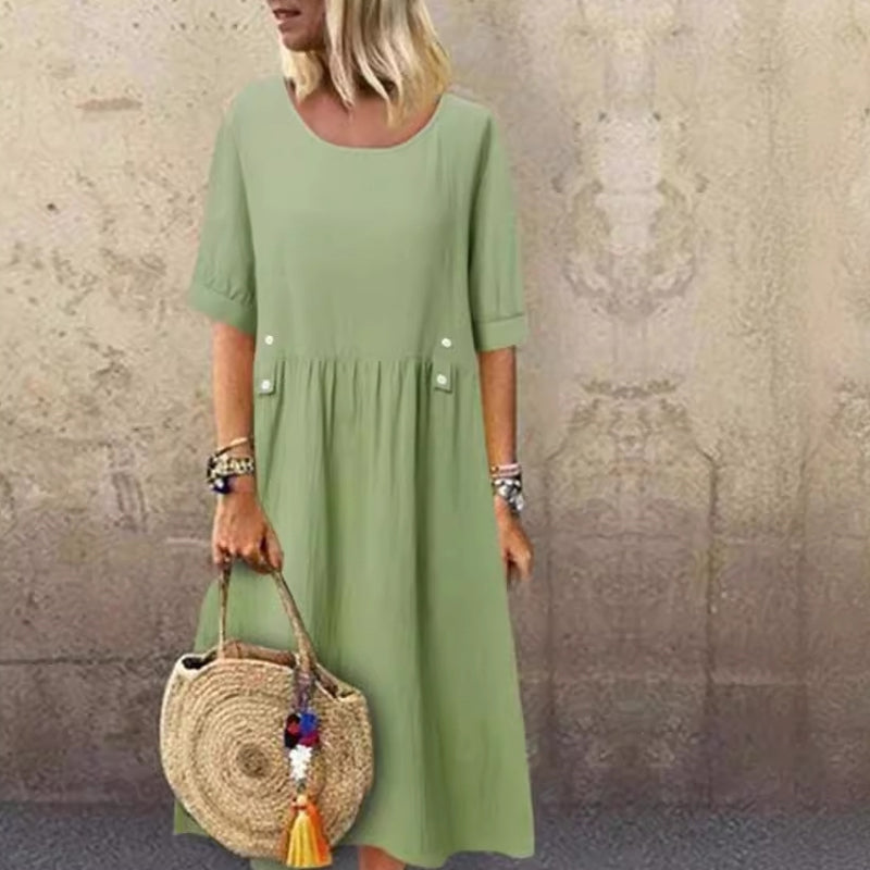 Donna con abito verde chiaro, borsa di paglia rotonda, sfondo muro beige. Moda estiva casual, accessori colorati, stile boho chic.