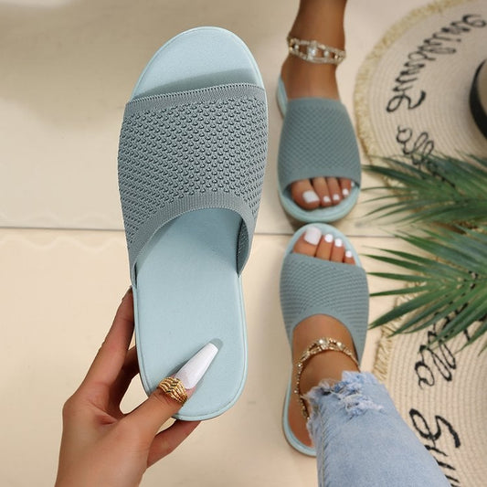 Sandali estivi azzurri in maglia, indossati su pavimento chiaro. Dettaglio di pedicure bianca e jeans strappati. Accessori moda estivi.