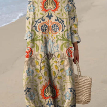 Abito lungo boho con motivo floreale colorato, indossato su spiaggia sabbiosa. Stile estivo, tessuto leggero, borsa di paglia intrecciata.