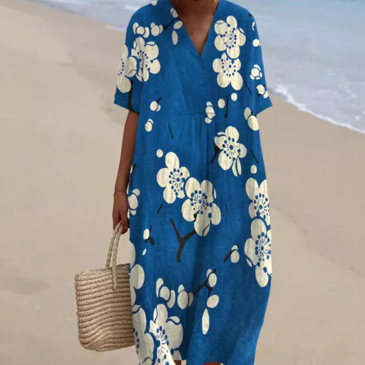 Abito estivo blu con fiori bianchi, maniche corte, indossato su spiaggia sabbiosa. Donna con borsa di paglia. Moda mare, abbigliamento estivo.