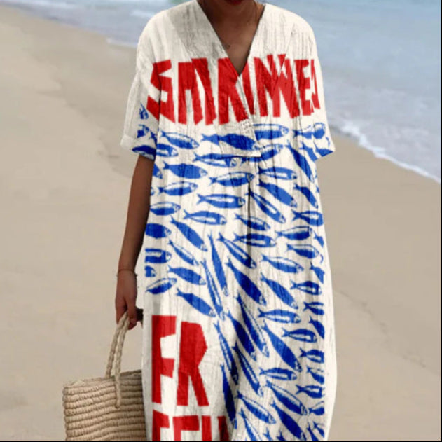 Abito estivo bianco con scritta rossa "Sardines" e motivi blu di pesci, indossato su spiaggia sabbiosa. Borsa di paglia intrecciata.