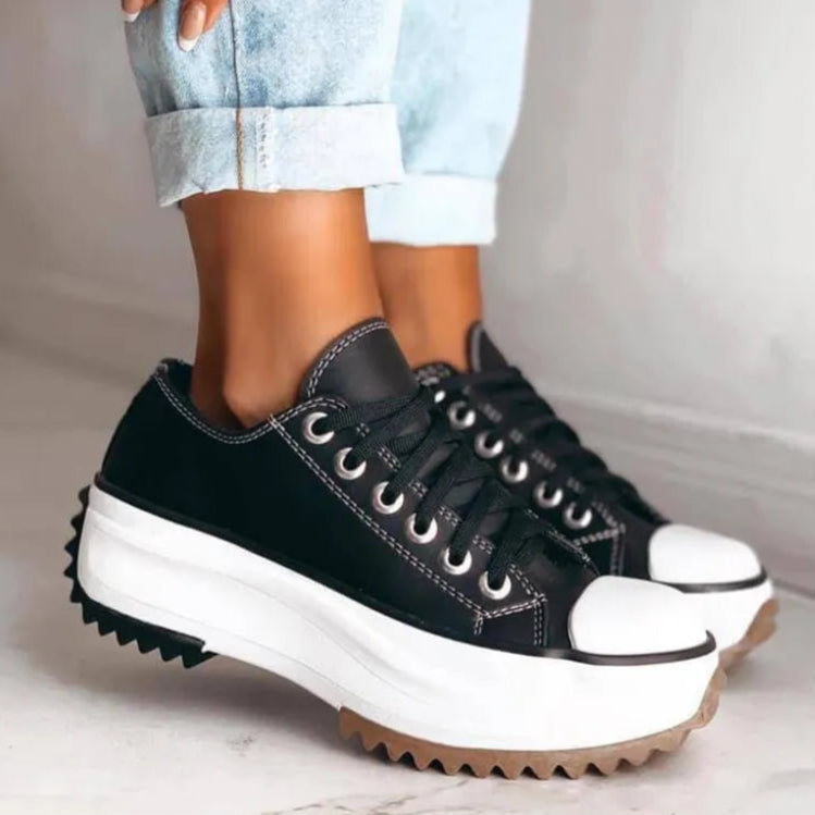 Scarpe da ginnastica nere con suola spessa bianca e dettagli in gomma marrone, indossate con jeans chiari risvoltati. Moda casual, calzature trendy.