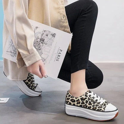 Scarpe da ginnastica leopardate con suola alta indossate da una persona in jeans neri, che tiene una rivista. Moda urbana, calzature trendy.