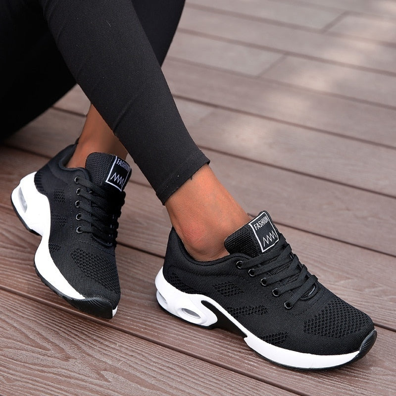 Scarpe da ginnastica nere da donna su pavimento in legno, design moderno e traspirante, ideali per sport e tempo libero.