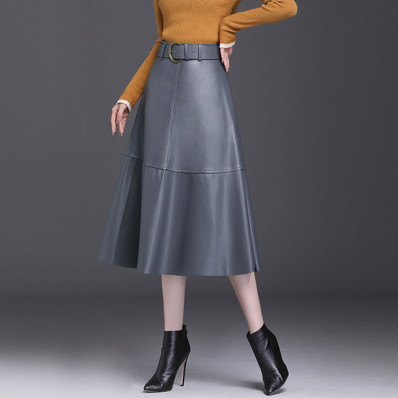 Donna con gonna in pelle grigia a vita alta, maglione arancione e stivaletti neri con tacco. Moda autunnale elegante e sofisticata.