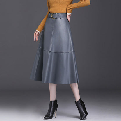 Donna con gonna in pelle grigia a vita alta, maglione arancione e stivaletti neri con tacco. Moda autunnale elegante e sofisticata.