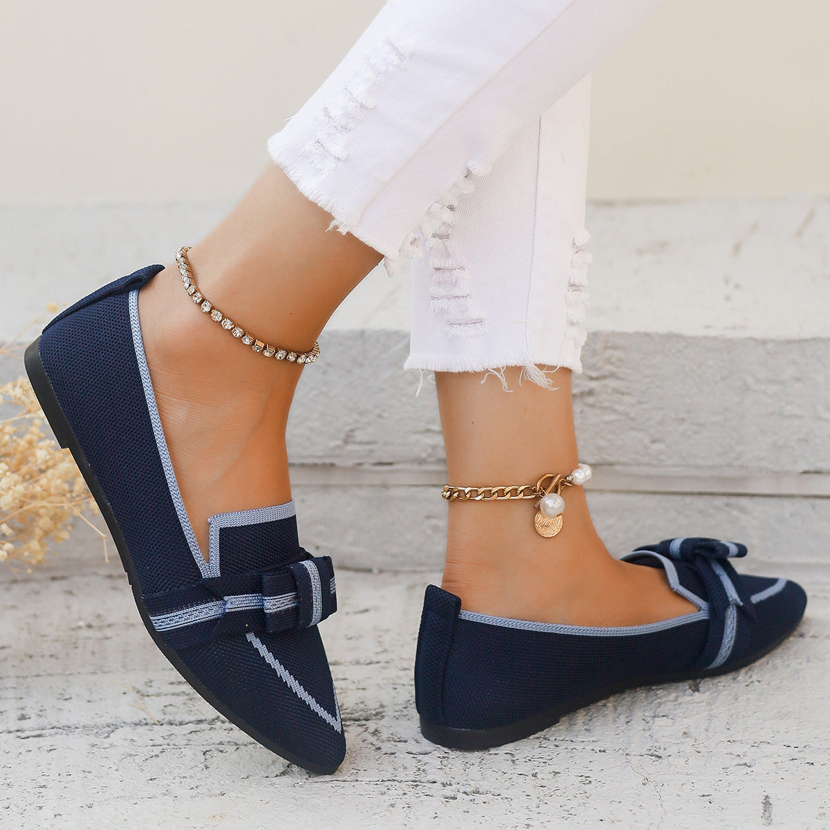 Scarpe mocassini blu scuro con fiocco, indossate con jeans bianchi strappati. Accessori: cavigliere dorate e argentate. Moda casual elegante.