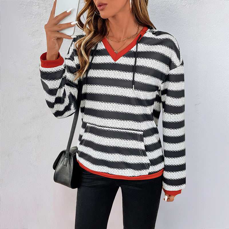 Donna con maglione a righe bianche e nere, scollo a V rosso, borsa nera, sfondo bianco. Moda casual autunnale, abbigliamento femminile trendy.