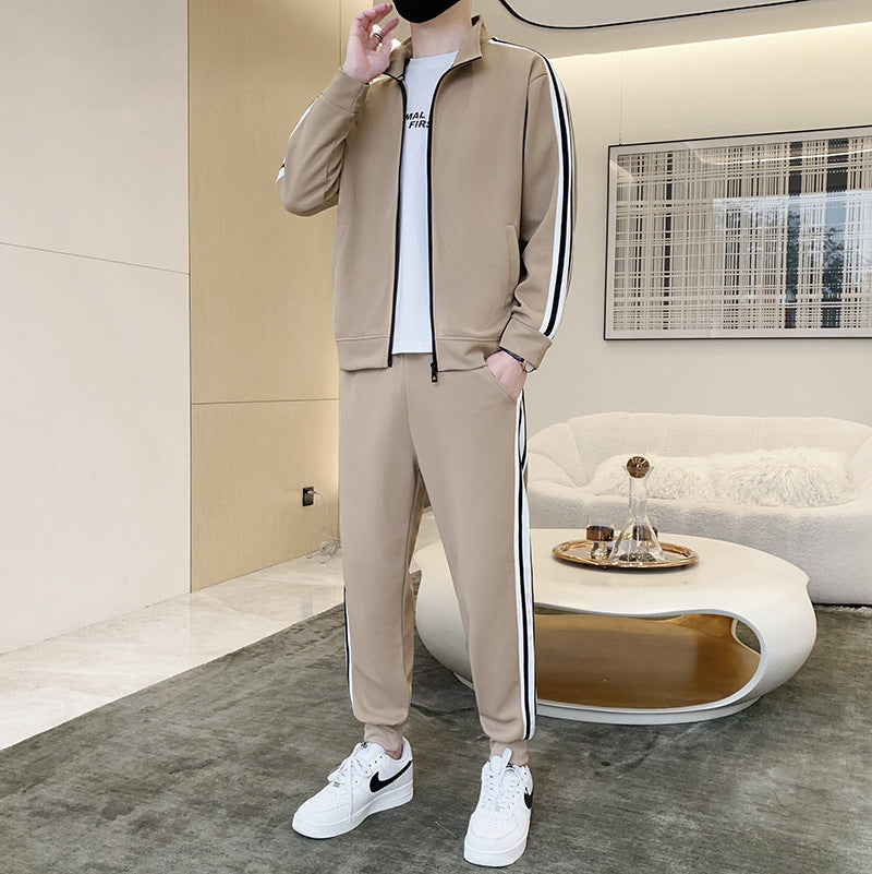 Tuta sportiva beige con strisce bianche e nere, indossata con scarpe da ginnastica bianche Nike, in un salotto moderno con divano e tavolino.