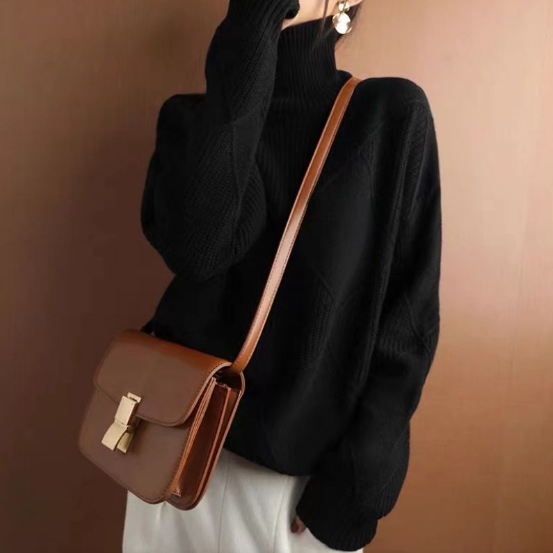 Donna con maglione nero a collo alto e borsa a tracolla marrone, moda autunno inverno, stile casual chic, sfondo marrone.