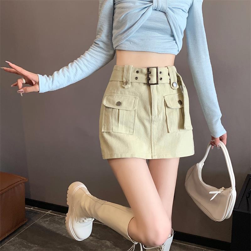 Donna con top azzurro e gonna beige a vita alta, stivali bianchi e borsa a mano. Moda femminile autunnale, outfit casual chic.