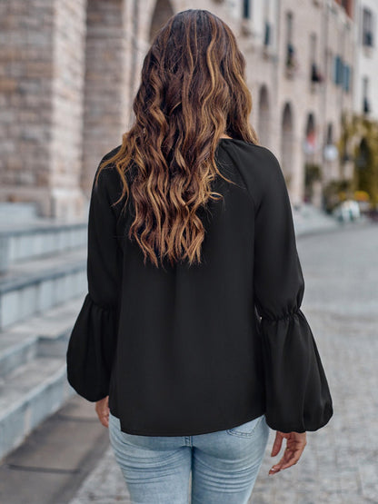 Donna con capelli ondulati lunghi, indossa camicetta nera e jeans, cammina su strada di pietra in città storica. Moda casual autunnale.