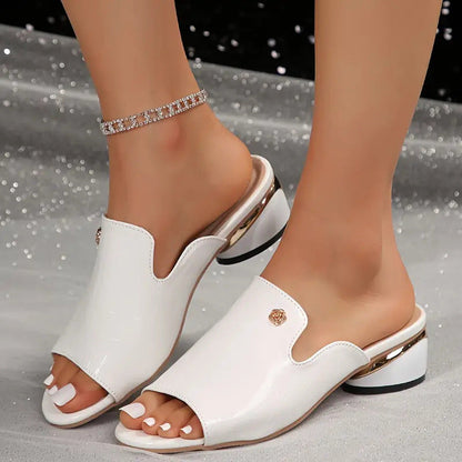 Sandali bianchi eleganti con tacco basso e dettagli dorati, indossati su piedi femminili con cavigliera brillante. Moda estiva, calzature chic.