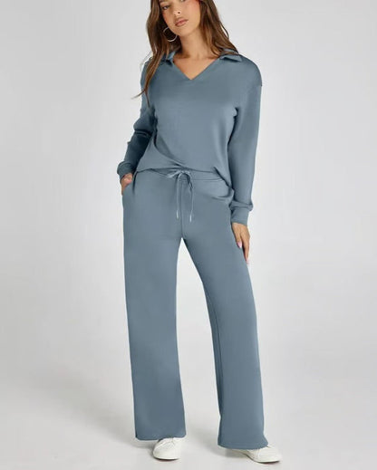 Donna in tuta sportiva blu, con cappuccio e pantaloni larghi, mani in tasca, su sfondo bianco. Abbigliamento casual, moda donna, comfort.