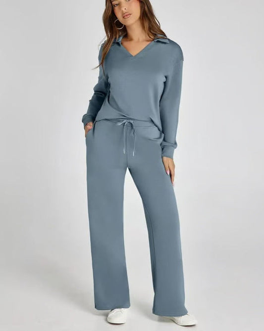 Donna in tuta sportiva blu, con cappuccio e pantaloni larghi, mani in tasca, su sfondo bianco. Abbigliamento casual, moda donna, comfort.