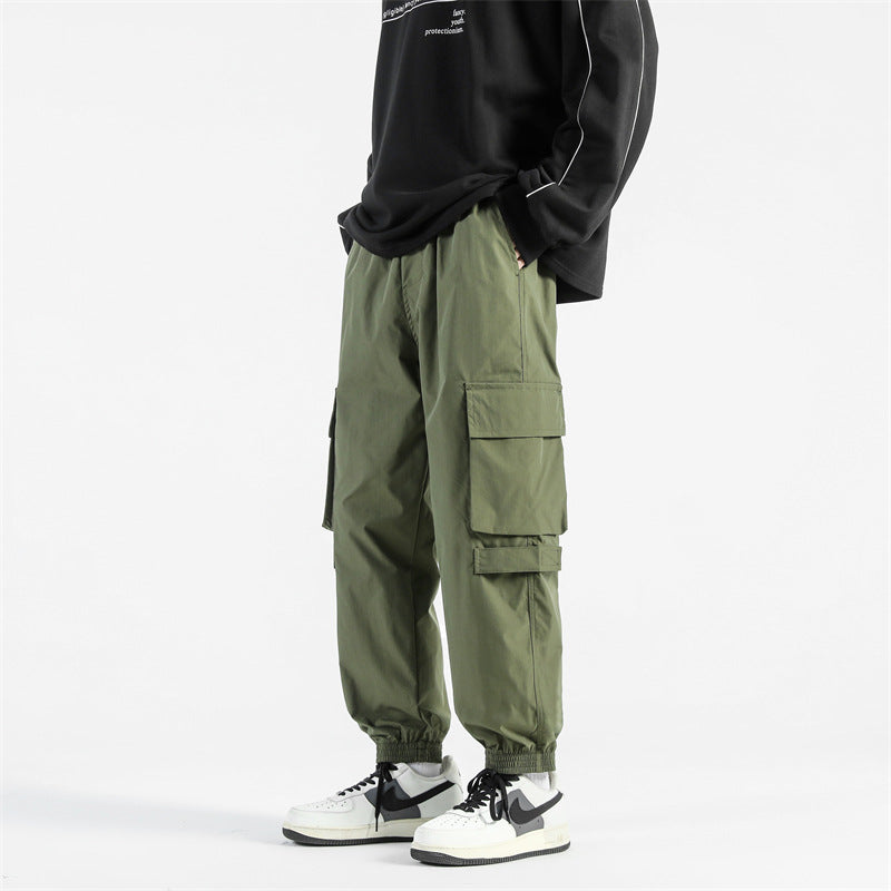 Pantaloni cargo verdi da uomo, stile casual, con tasche multiple, abbinati a sneakers bianche e nere e felpa nera. Moda streetwear.