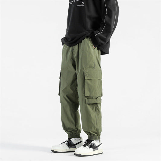 Pantaloni cargo verdi da uomo, stile casual, con tasche multiple, abbinati a sneakers bianche e nere e felpa nera. Moda streetwear.