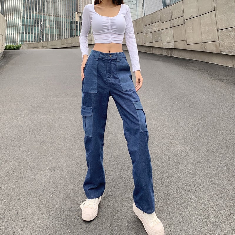 Donna con top bianco a maniche lunghe e jeans cargo blu su strada urbana. Moda casual, stile streetwear, pantaloni larghi, scarpe da ginnastica bianche.