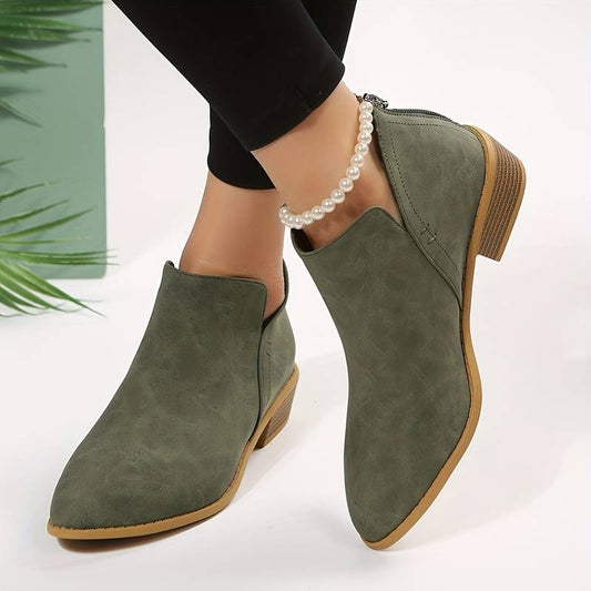 Stivaletti verdi da donna in pelle scamosciata, tacco basso, indossati con pantaloni neri e cavigliera di perle. Moda autunnale elegante.