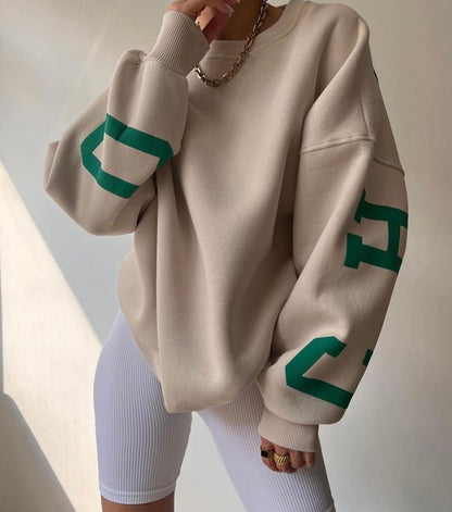 Donna con felpa beige oversize, dettagli verdi, indossa pantaloncini bianchi a coste. Look casual e moderno, moda streetwear femminile.