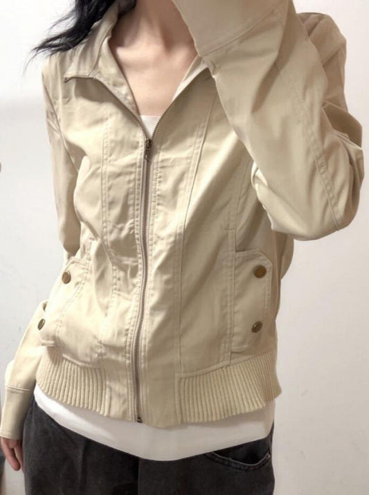 Giacca beige da donna con zip frontale, tasche con bottoni, indossata sopra maglietta bianca. Moda casual, abbigliamento autunnale.