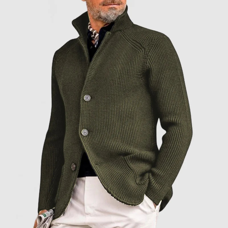 Uomo con giacca cardigan verde oliva, bottoni grandi, camicia nera, pantaloni chiari. Moda maschile elegante, stile autunnale casual.