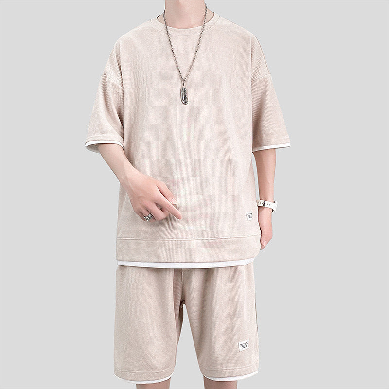 Uomo in abbigliamento casual beige, indossa maglietta e pantaloncini coordinati, collana e orologio. Moda estiva, stile minimalista.