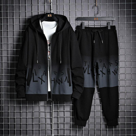 Tuta sportiva nera e grigia con cappuccio, design moderno, lettere stampate, appesa su griglia metallica. Abbigliamento casual uomo.