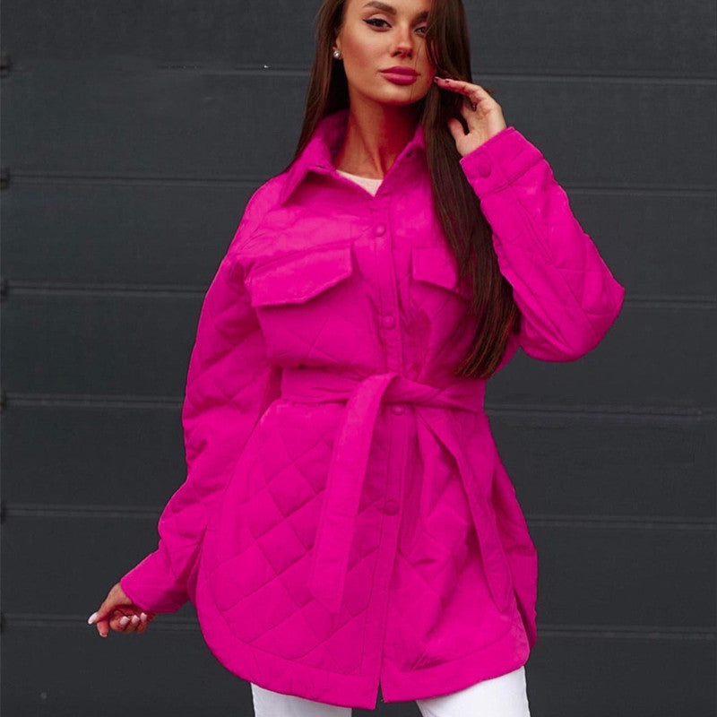 Donna con giacca trapuntata fucsia, cintura in vita, sfondo nero. Moda autunno inverno, abbigliamento femminile elegante e colorato.