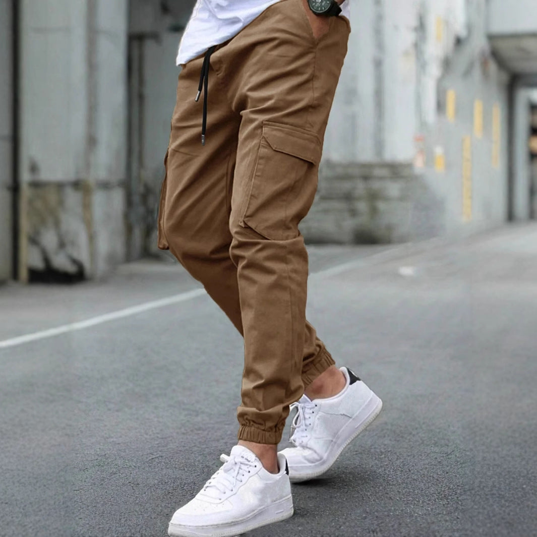 Pantaloni cargo marroni da uomo, stile casual, con tasche laterali, abbinati a scarpe da ginnastica bianche su strada urbana.