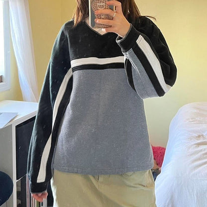 Donna che indossa una felpa oversize grigia e nera con strisce bianche, scatta un selfie allo specchio in una stanza luminosa. Moda casual, abbigliamento comodo.