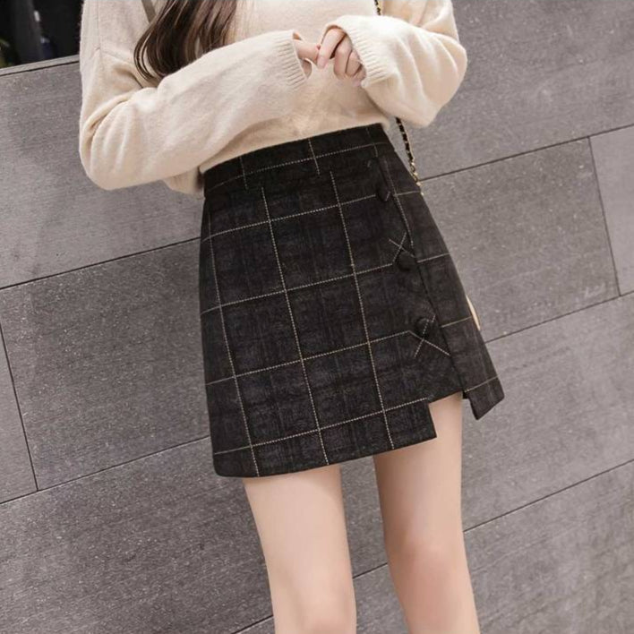 Donna con maglione beige e gonna scozzese nera, design asimmetrico, bottoni decorativi. Moda autunnale, abbigliamento casual elegante.
