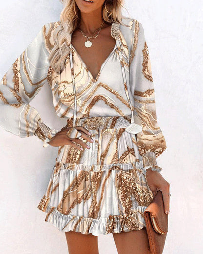 Donna con abito elegante a fantasia marmo beige e bianco, maniche lunghe, gonna a balze, collana dorata, borsa marrone. Moda femminile chic.