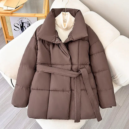 Giacca imbottita marrone con cintura, design trapuntato, su sedia bianca. Moda invernale, abbigliamento caldo, stile casual elegante.