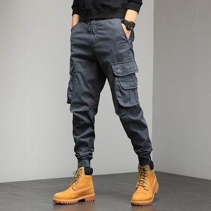 Pantaloni cargo grigi da uomo con tasche multiple, abbinati a stivali gialli in pelle. Stile casual e moderno, ideale per moda urbana.