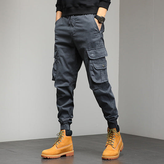 Pantaloni cargo grigi da uomo con tasche multiple, abbinati a stivali gialli in pelle. Stile casual e moderno, ideale per moda urbana.