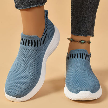 Scarpe da ginnastica blu senza lacci, suola bianca, indossate con jeans. Design traspirante, comode per camminare. Accessorio cavigliera turchese.