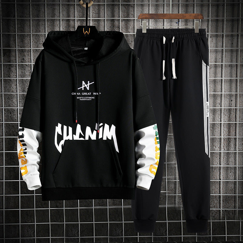 Set di abbigliamento sportivo nero, felpa con cappuccio e pantaloni, design moderno con scritte bianche e dettagli colorati, appeso su griglia metallica.