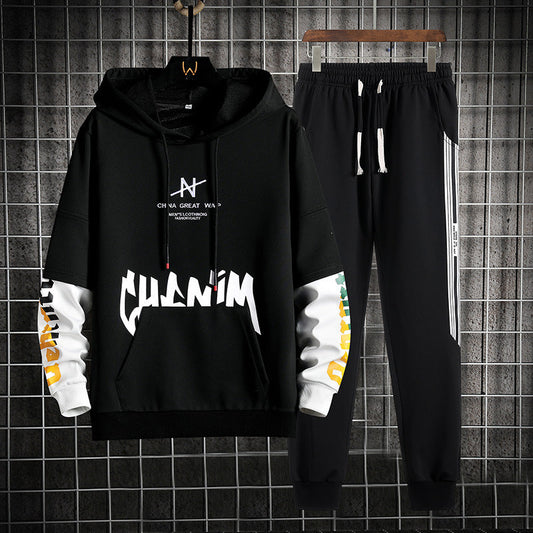 Set di abbigliamento sportivo nero, felpa con cappuccio e pantaloni, design moderno con scritte bianche e dettagli colorati, appeso su griglia metallica.