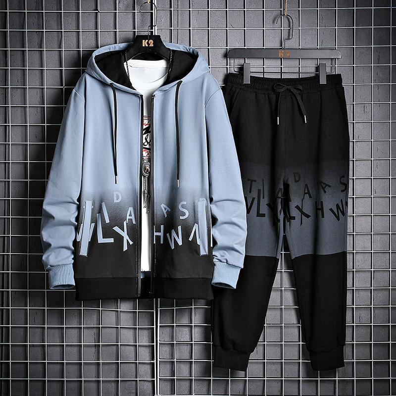 Tuta sportiva uomo, felpa con cappuccio blu e pantaloni neri, design moderno con lettere, appesa su griglia metallica. Abbigliamento casual trendy.