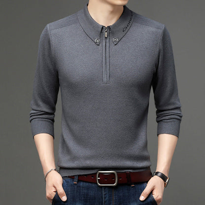 Maglione grigio da uomo con colletto alto e zip, abbinato a jeans blu e cintura marrone. Moda maschile elegante e casual.