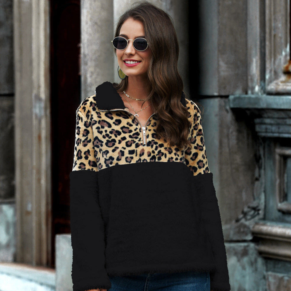 Donna con occhiali da sole indossa felpa leopardata e nera, sorridente davanti a edificio urbano. Moda autunnale, stile casual chic.