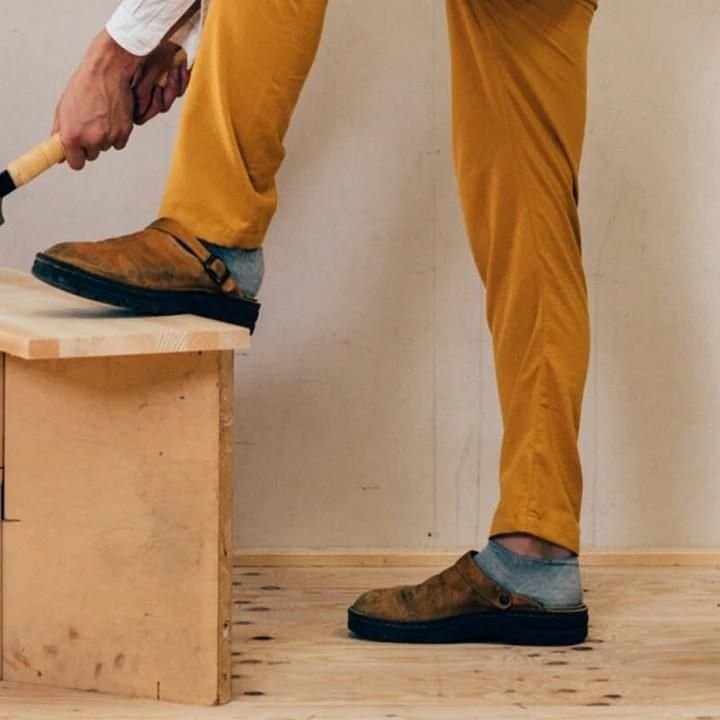 Uomo in pantaloni gialli e scarpe marroni usa un martello su una panca di legno. Lavoro artigianale, falegnameria, fai da te.