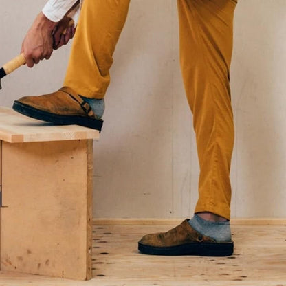 Uomo in pantaloni gialli e scarpe marroni usa un martello su una panca di legno. Lavoro artigianale, falegnameria, fai da te.