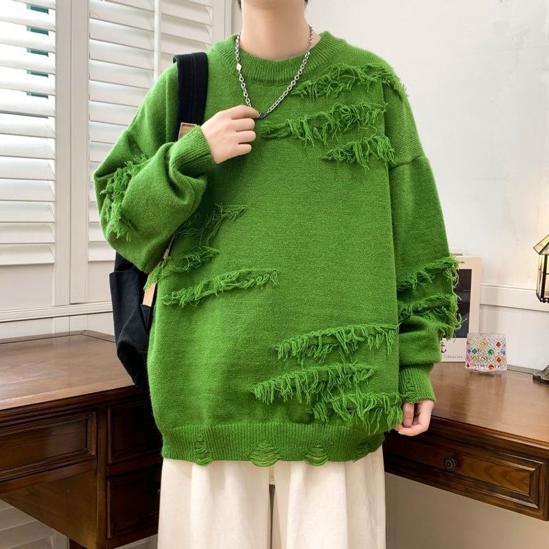 Maglione verde oversize con dettagli sfrangiati, indossato da una persona in una stanza con mobili in legno. Stile casual, moda autunnale.