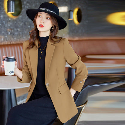 Donna elegante con cappello nero e blazer marrone, seduta in un caffè moderno, tiene una tazza da asporto. Moda autunnale, stile urbano chic.